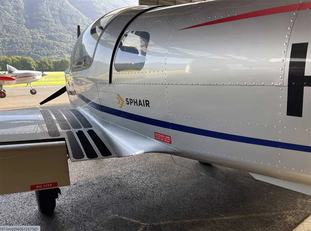 Close-up view of the silver fuselage of a Sonaca 200 aircraft with a blue stripe and "SPHAIR" text, parked outdoors.