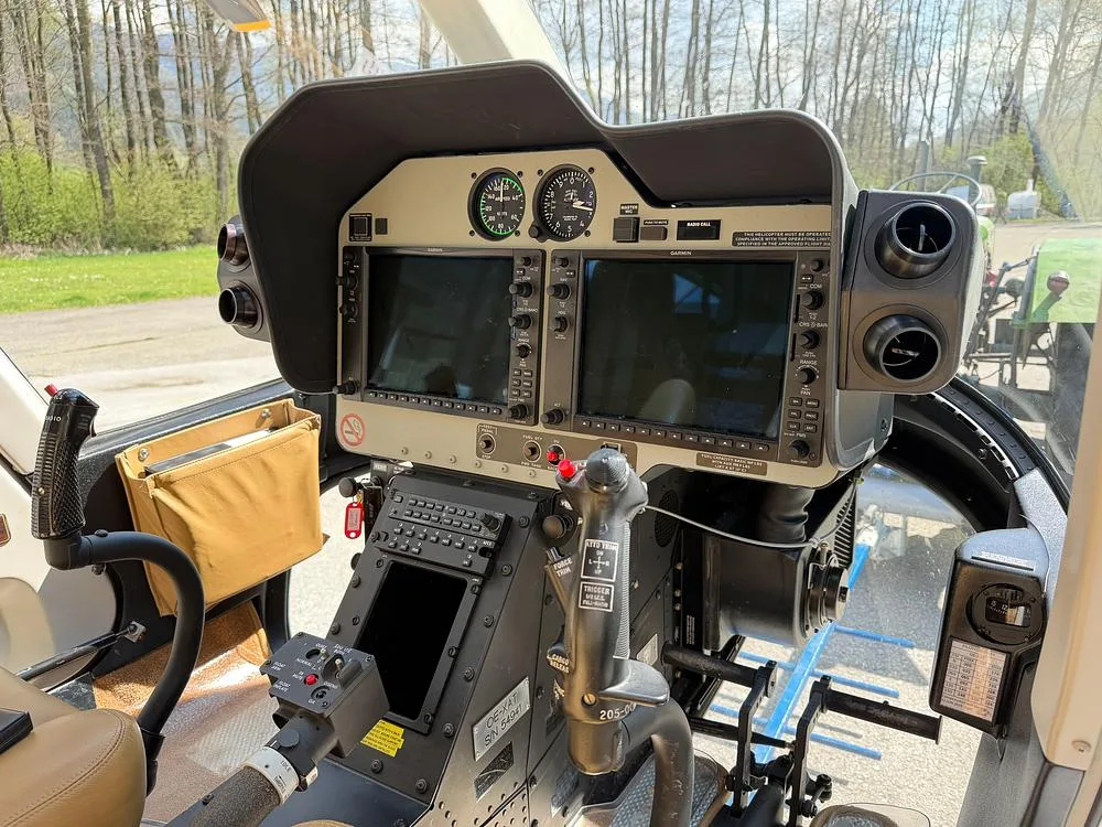 The cockpit of a helicopter features a dual-screen Garmin avionics system and flight controls.