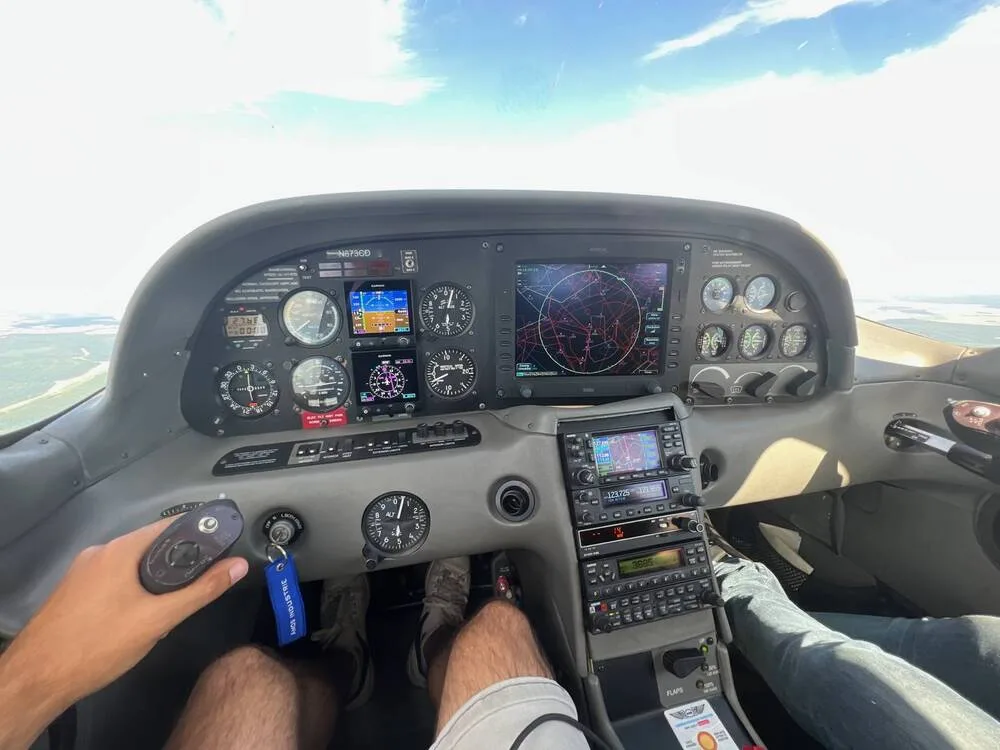 The cockpit of a Cirrus SR20 aircraft (N873CD) showing the instrument panel with multiple displays and controls, with a pilot's legs visible.