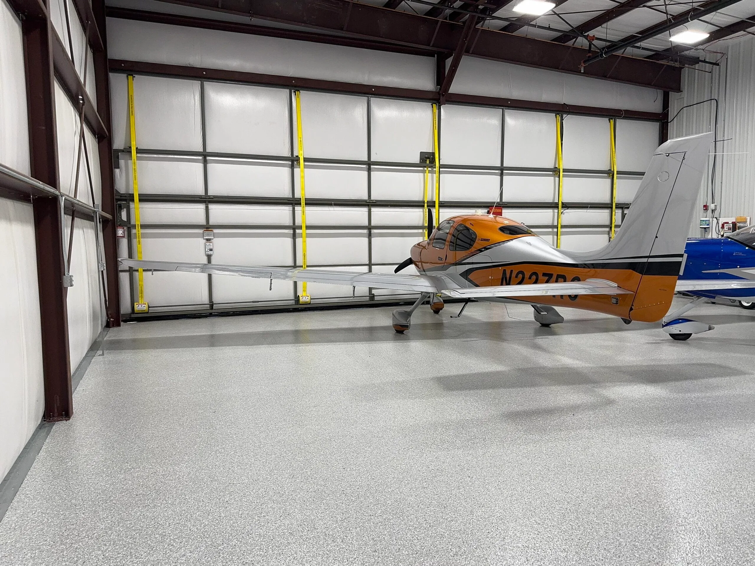 A Cirrus SR22 aircraft with orange and silver paint parked inside a hangar with a large closed door.