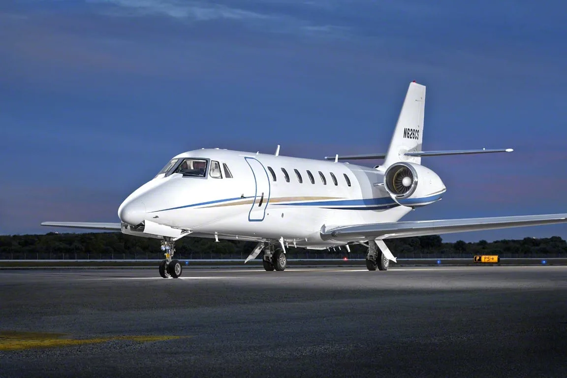 A white business jet with blue and gold stripes, registration N62601, parked on a tarmac at dusk.