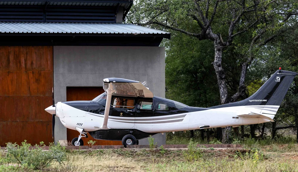 A black and white single-engine propeller aircraft is parked on a paved area next to a modern building with a metal roof.