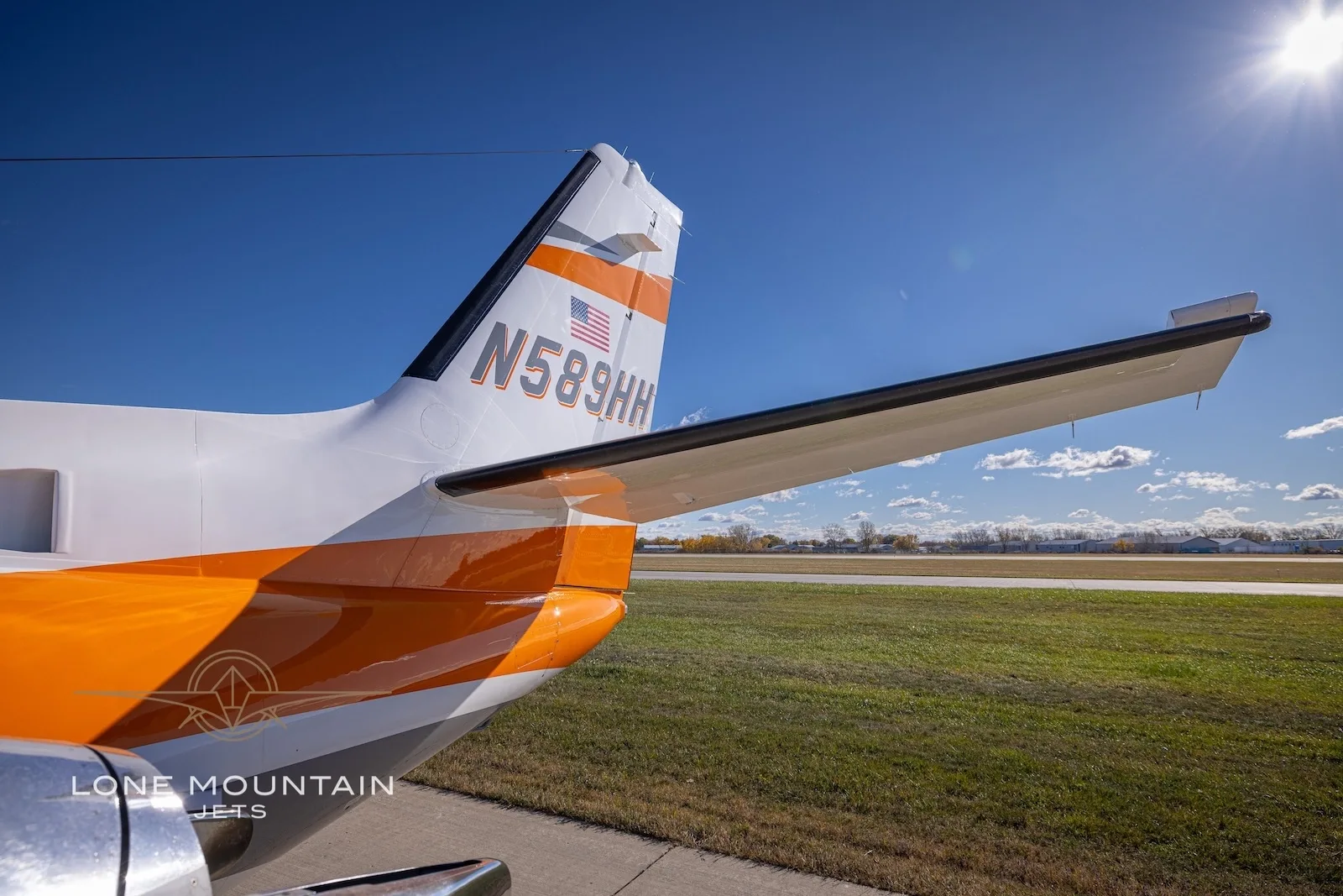 A close-up view of the tail of the Cessna Citation Bravo N589HH, showing the orange and grey stripe and US flag.