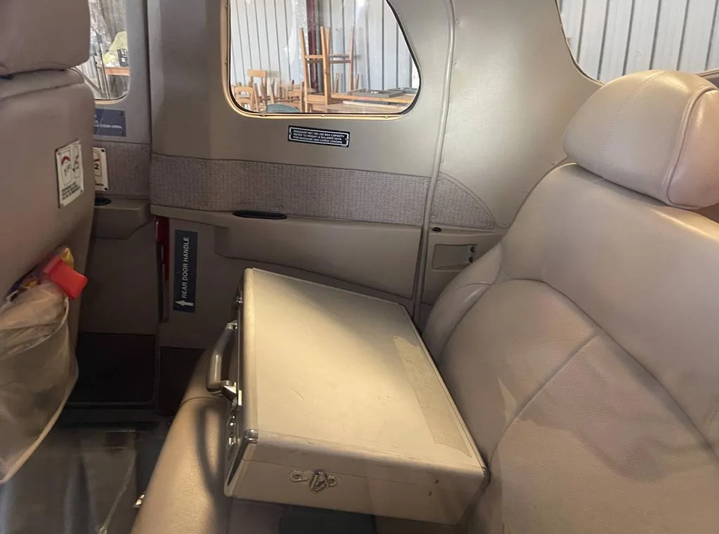 The beige leather interior of the aircraft cabin, showing rear seats and a silver briefcase.