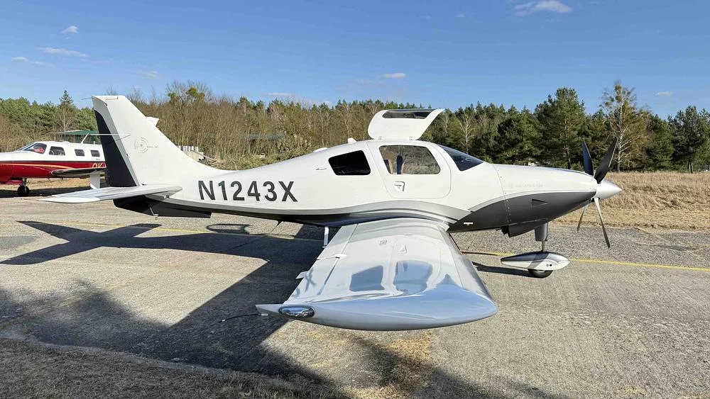 A white and grey Columbia 400 aircraft with registration N1243X parked on an airfield.