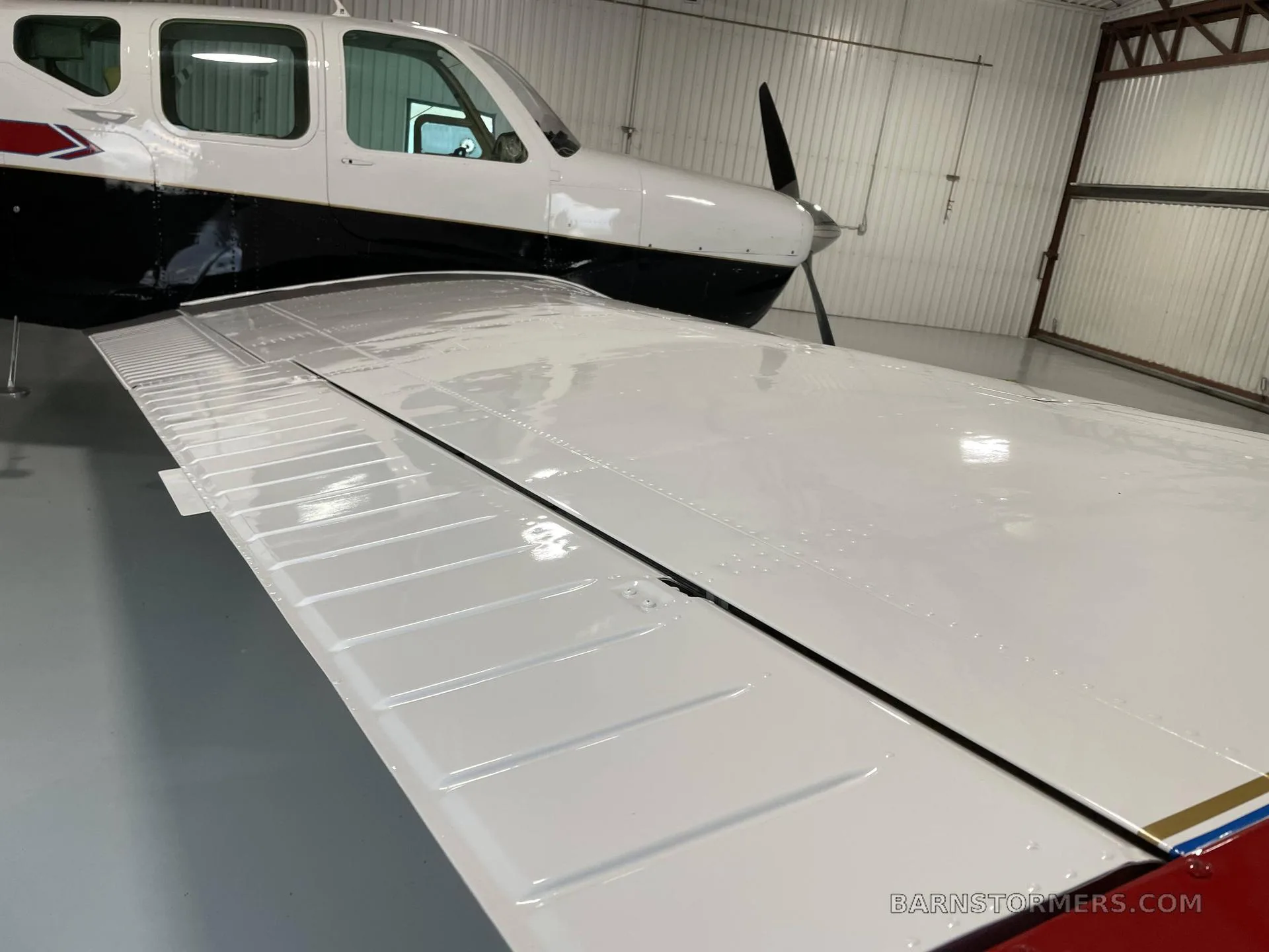 A close-up view of the white wing and black fuselage of a small aircraft inside a hangar.