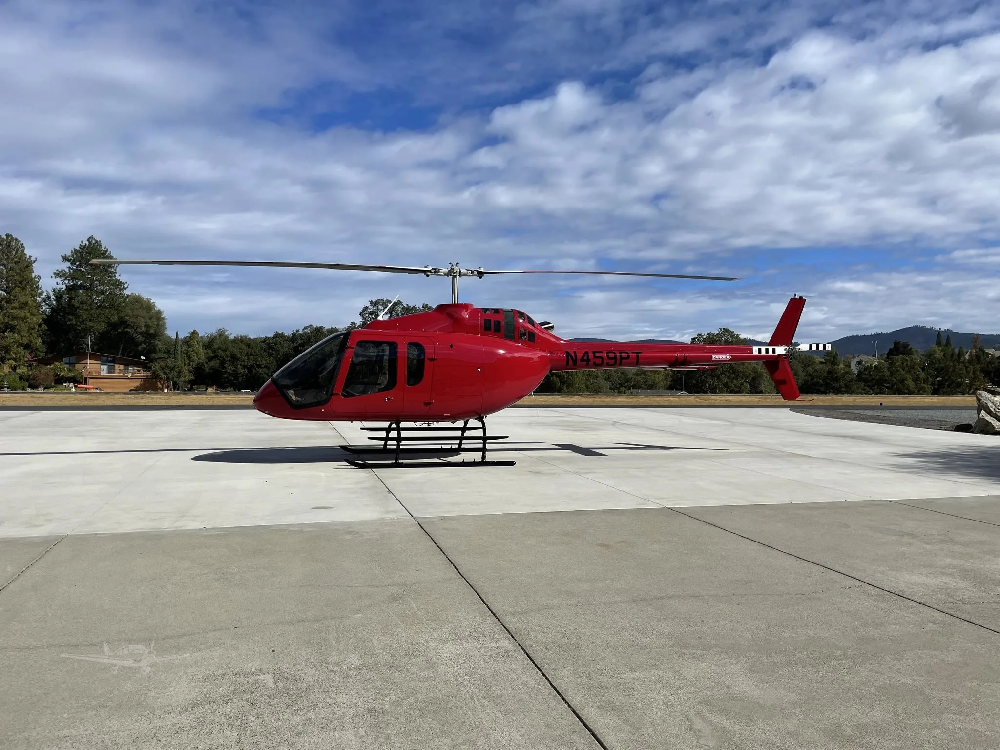 A red helicopter with tail number N459PT is parked on a concrete pad under a partly cloudy sky.