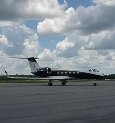 A Gulfstream G550 business jet with a black and white paint scheme is parked on an airport tarmac under a cloudy sky.