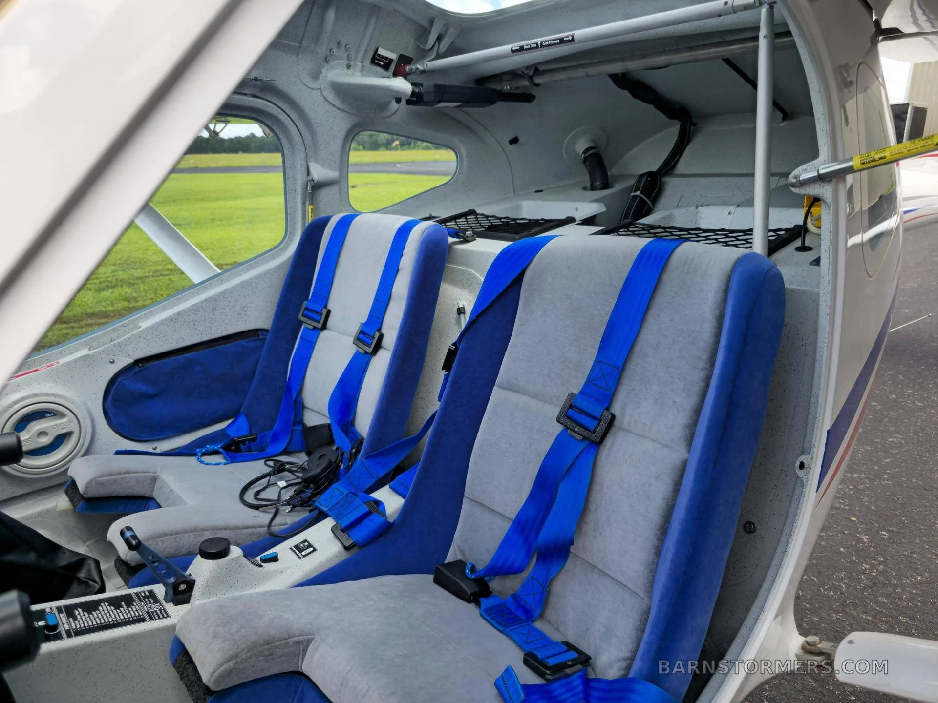 The interior of a light sport aircraft shows two grey and blue fabric seats with blue seatbelts.