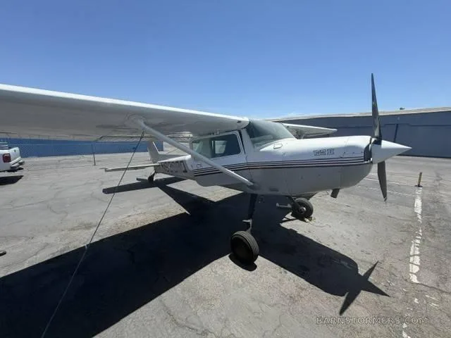 A white and grey single-engine propeller aircraft with a dark stripe on the fuselage, parked on an asphalt ramp under a clear blue sky.