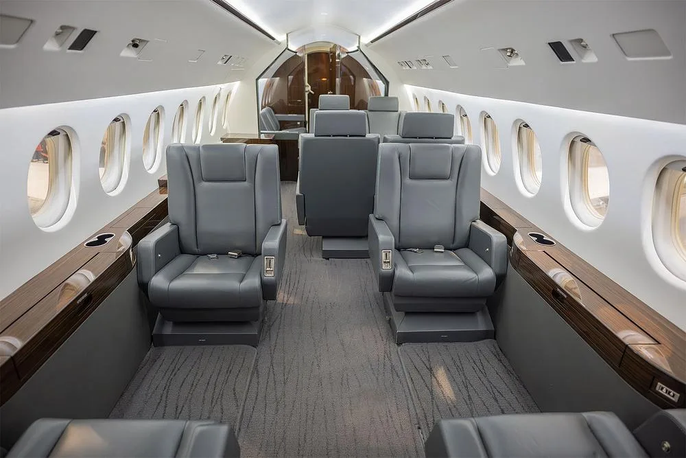 A view of the business jet's cabin interior, showing multiple grey leather seats and elegant wood paneling.