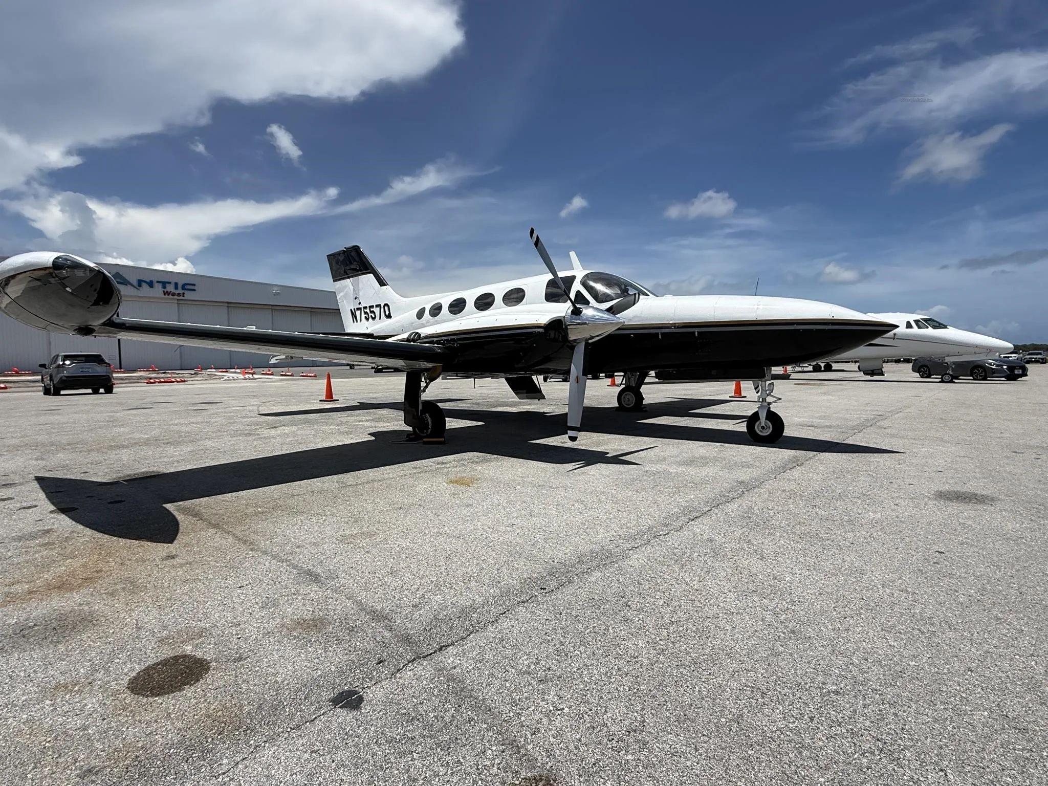 A white and black twin-engine Cessna 414 Chancellor aircraft (N7567Q) is parked on an asphalt tarmac under a partly cloudy sky.