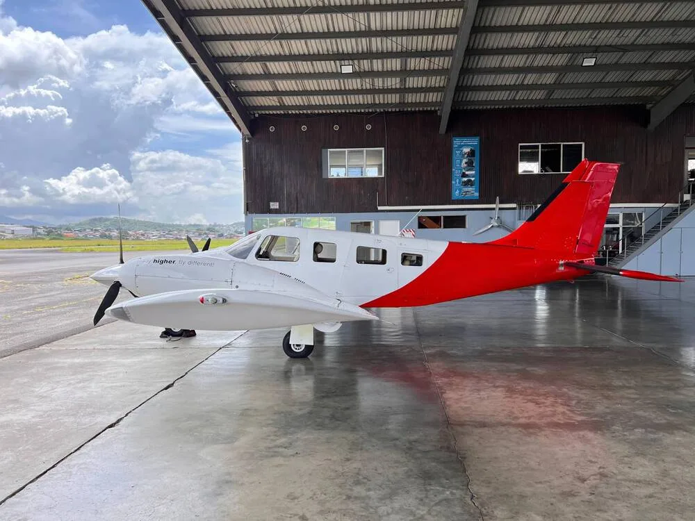 A white and red twin-engine propeller aircraft parked under a hangar, viewed from the side.