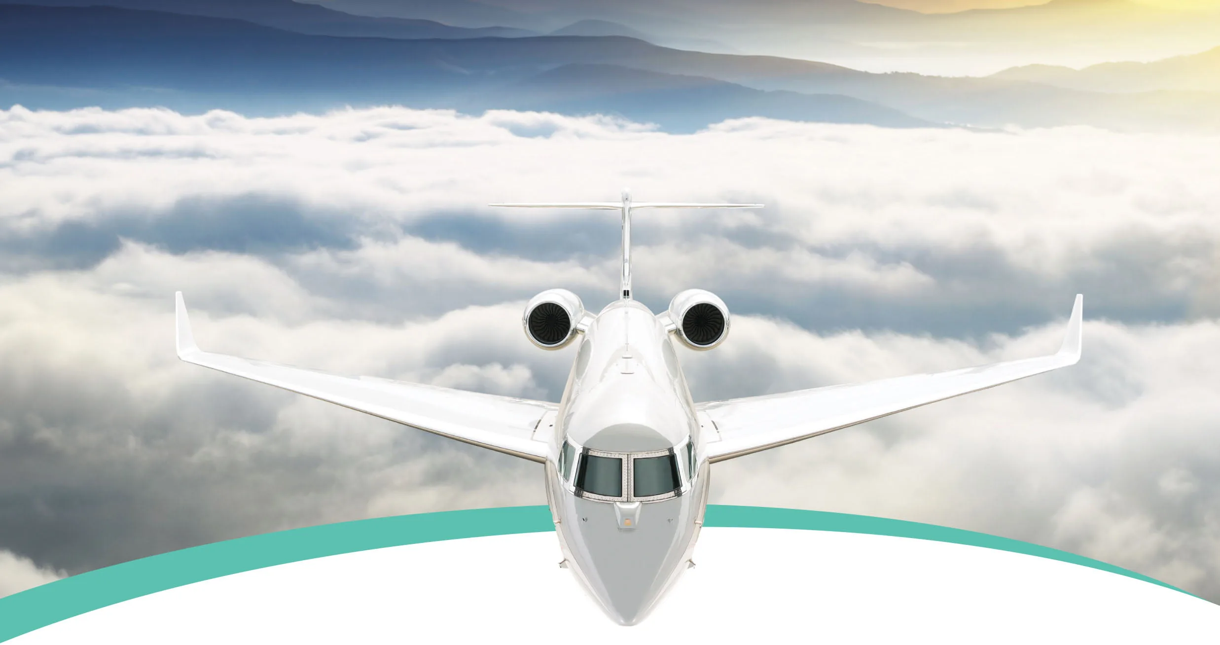 A white business jet flies head-on above clouds with mountains in the background.