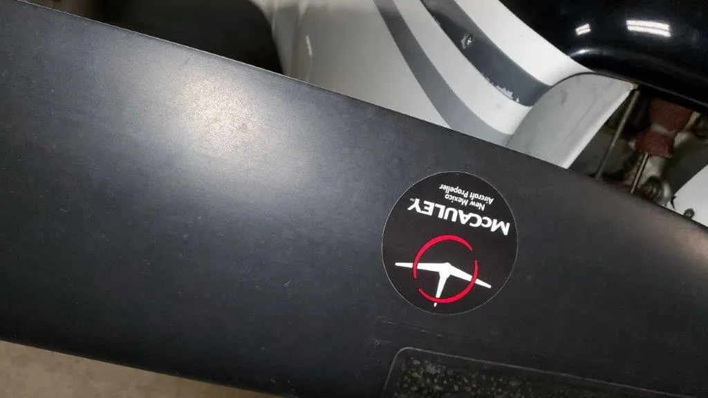 Close-up of a black aircraft propeller blade with a round McCauley sticker.