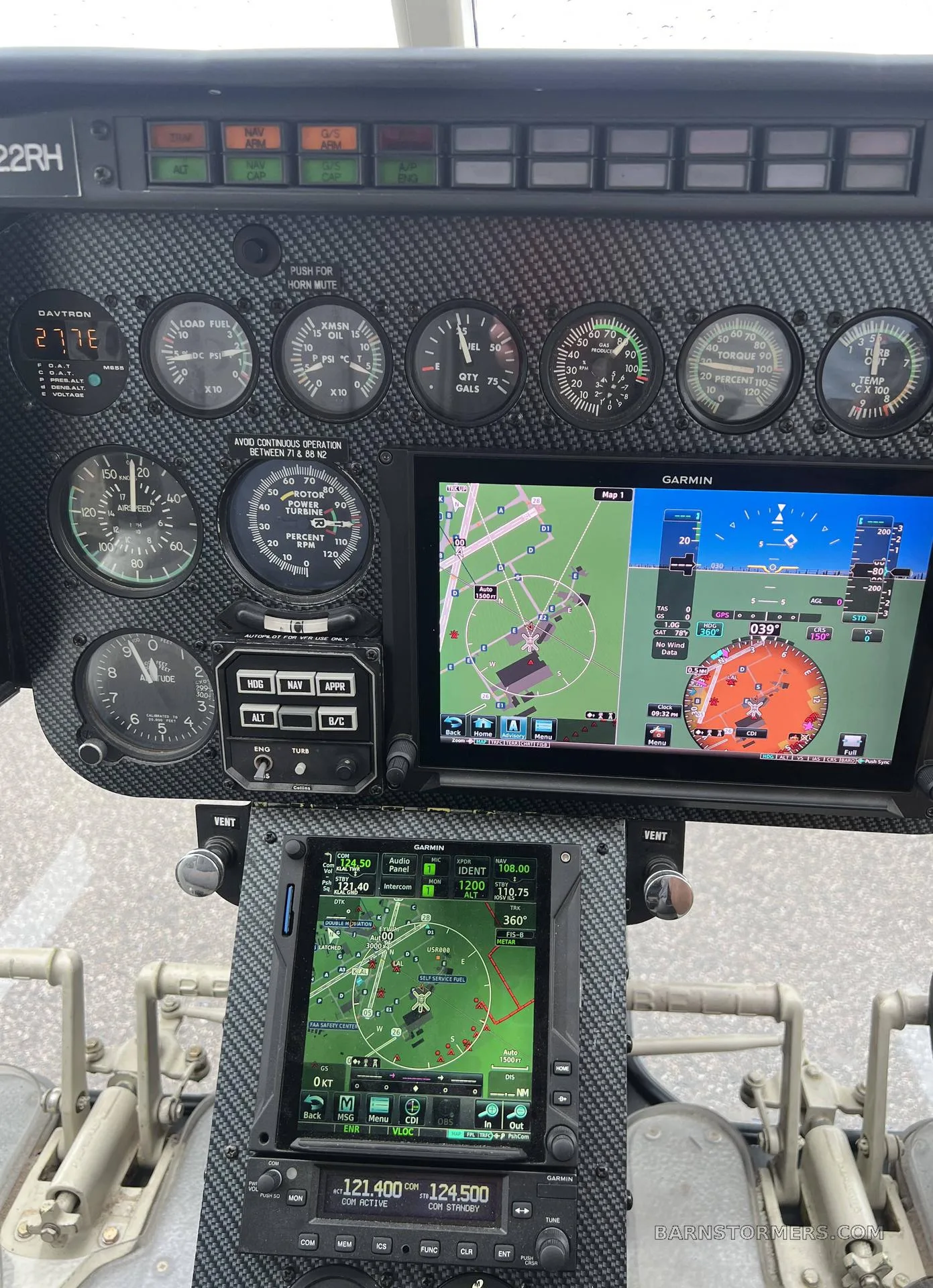 Close-up view of the Bell 206 helicopter's instrument panel with analog gauges and two Garmin digital displays.