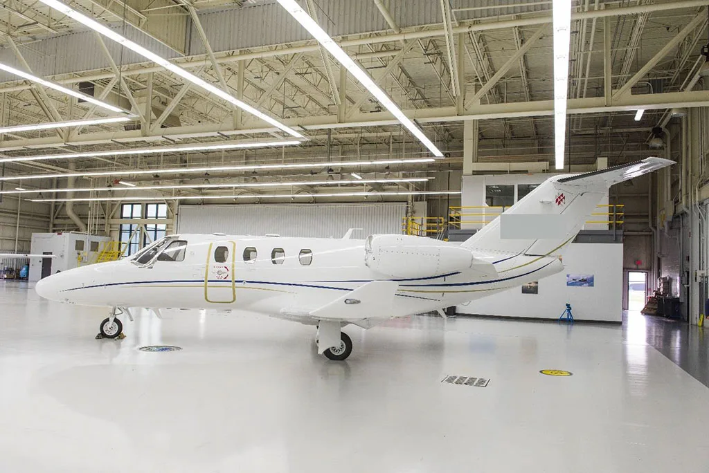 A white private jet with blue and gold stripes parked inside a brightly lit hangar.