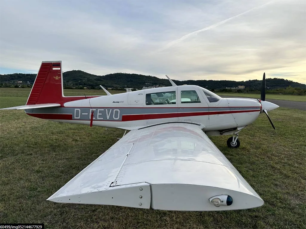 A white and red Mooney M20J aircraft (D-EEVO) seen from the front-right, parked on a grassy field.