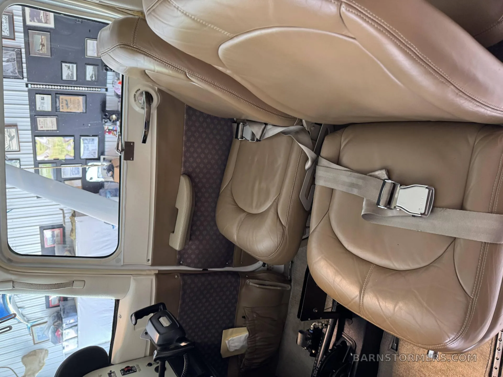The aircraft cabin features tan leather seats with seatbelts and a view of the wing through the window.