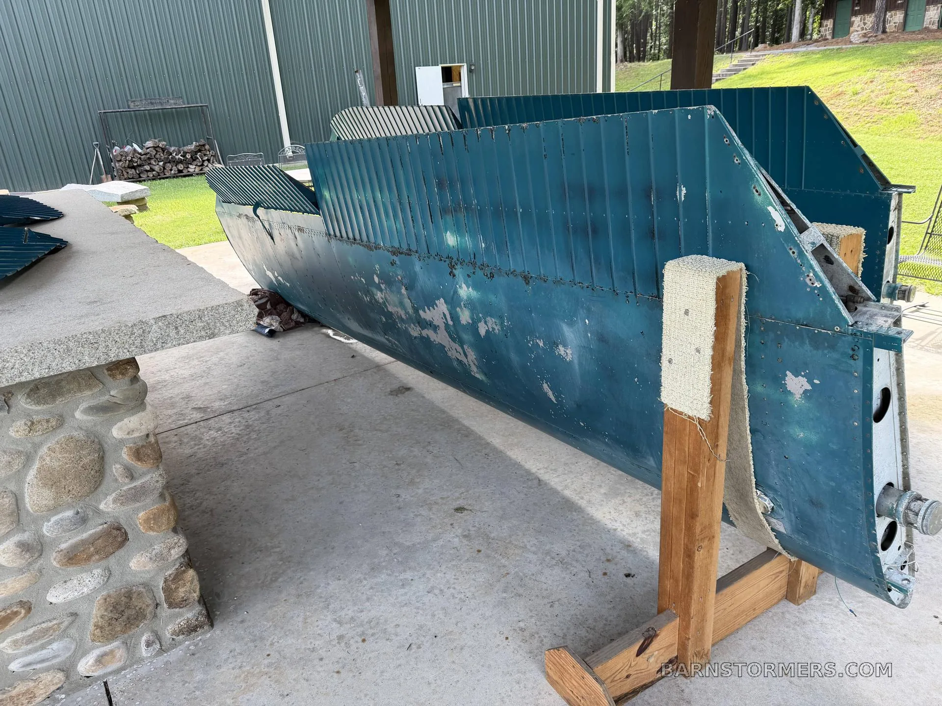 A large teal aircraft wing section, showing some wear, resting on wooden stands on a concrete patio.