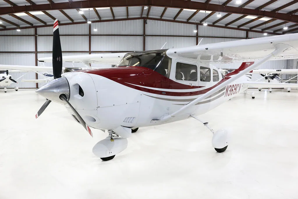 A white and red Cessna Stationair TC aircraft (N369CV) is parked in a hangar, viewed from the front left.