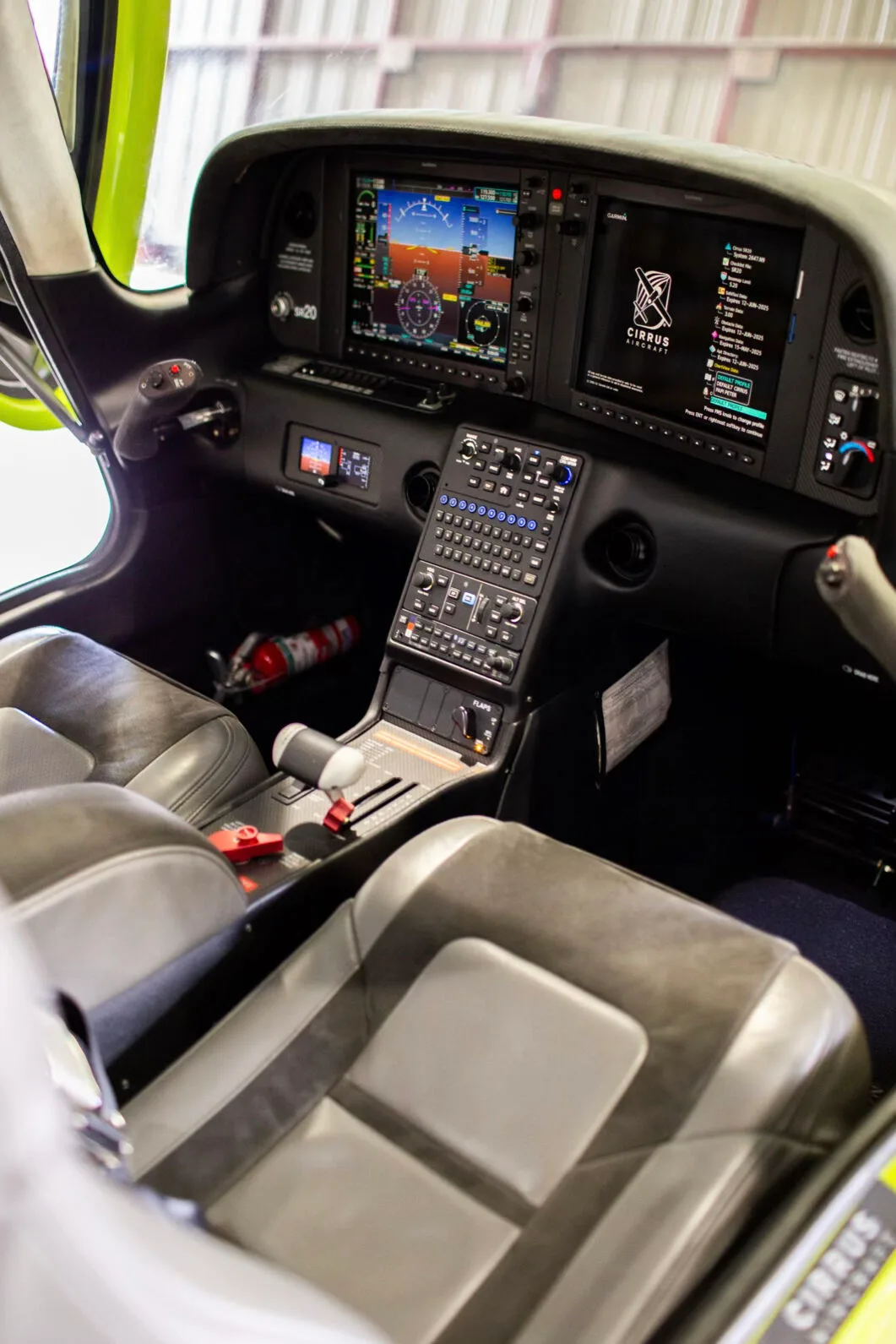 View of the Cirrus SR20 cockpit with dual screens, control panel, and gray leather seats.
