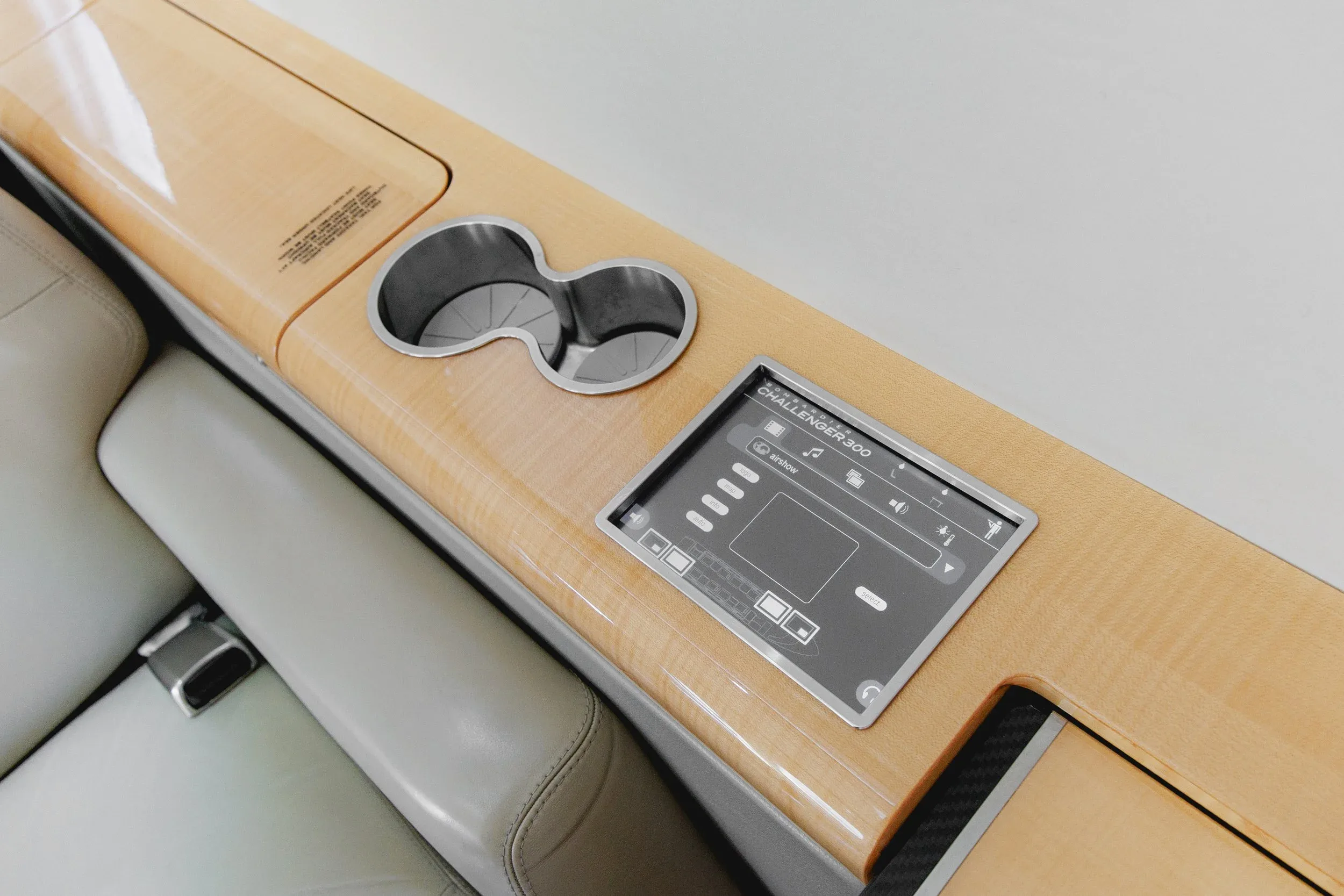 A close-up of a control panel and two cup holders integrated into the light wood side panel of a private jet cabin.