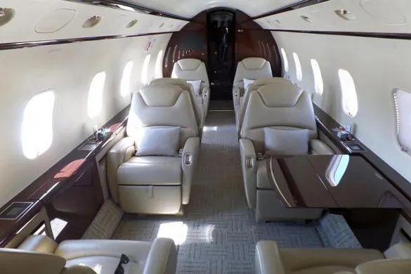 The luxurious interior cabin of a private jet with beige leather seats and dark wood accents.