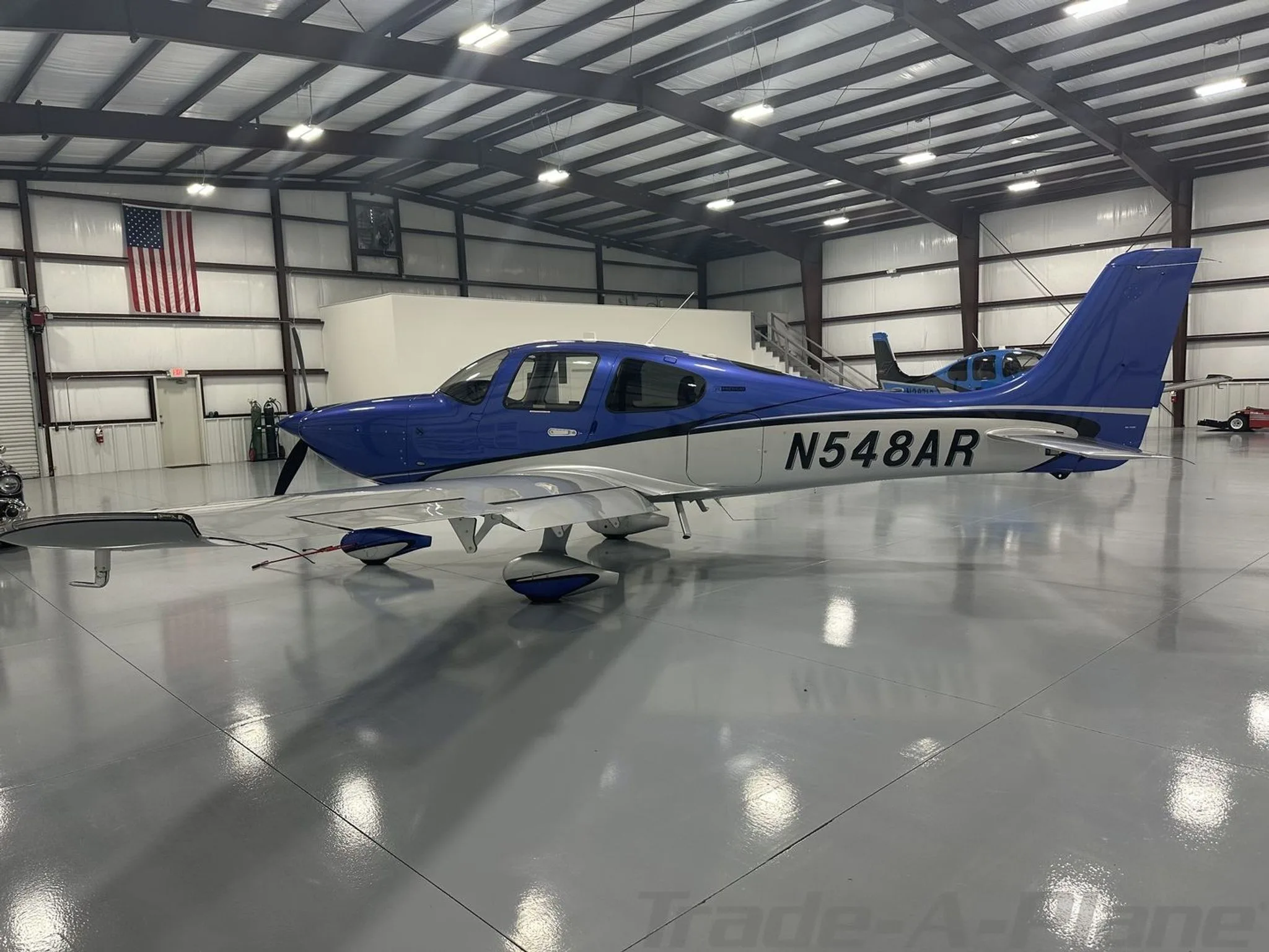 A blue and silver Cirrus SR22 aircraft with tail number N548AR parked in a hangar.