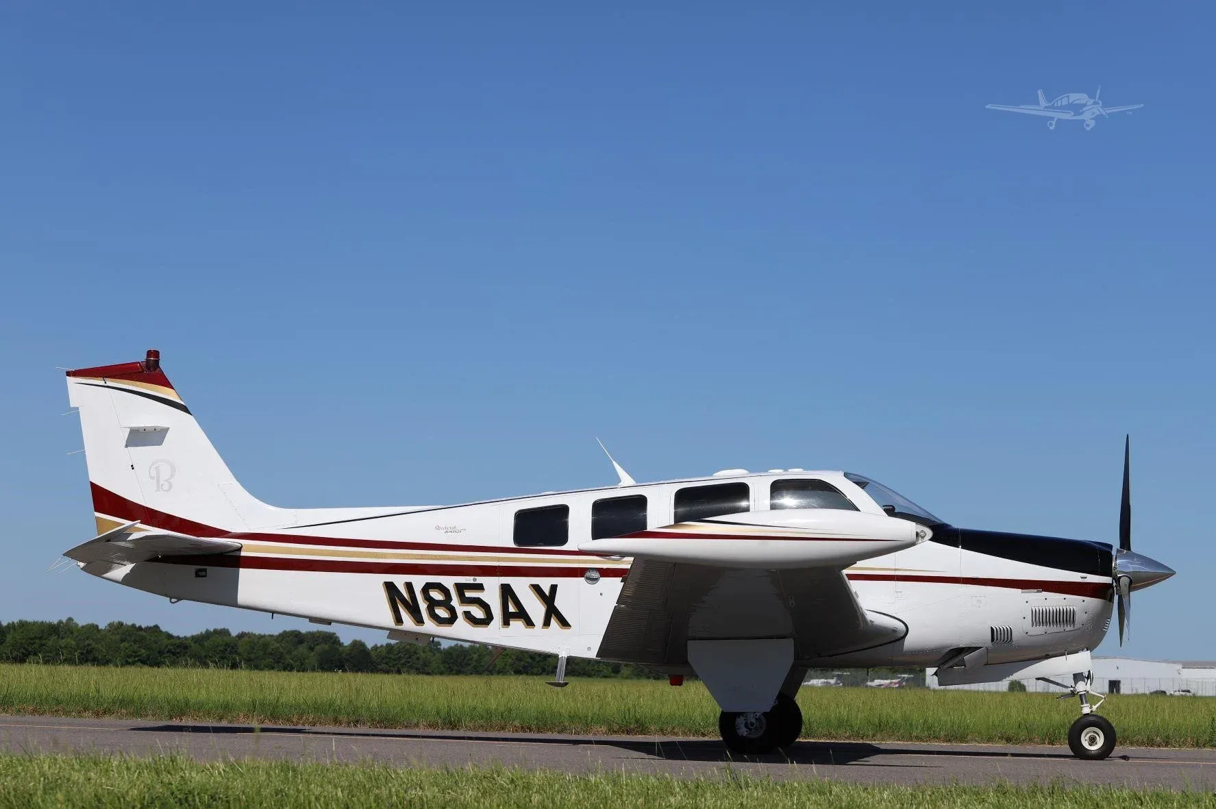 A white and black single-engine propeller aircraft with red and gold stripes and registration N85AX, viewed from the right side on a tarmac.