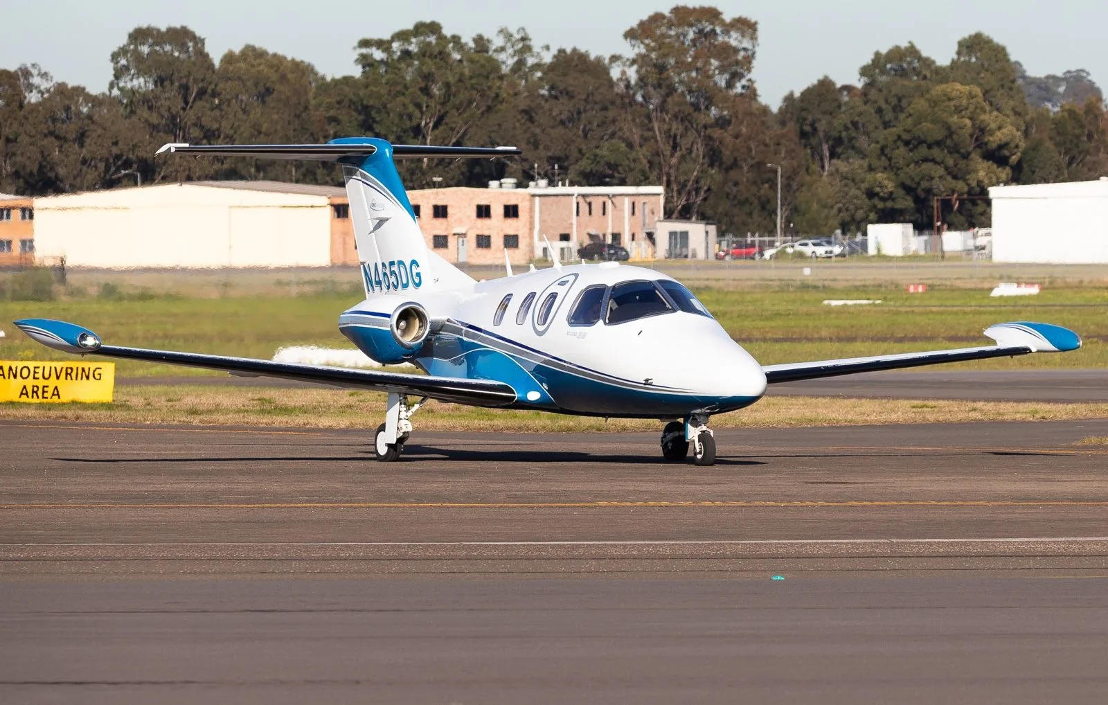 A white and blue Eclipse 500 jet, tail number N465DG, is seen on a tarmac with buildings and trees in the background.