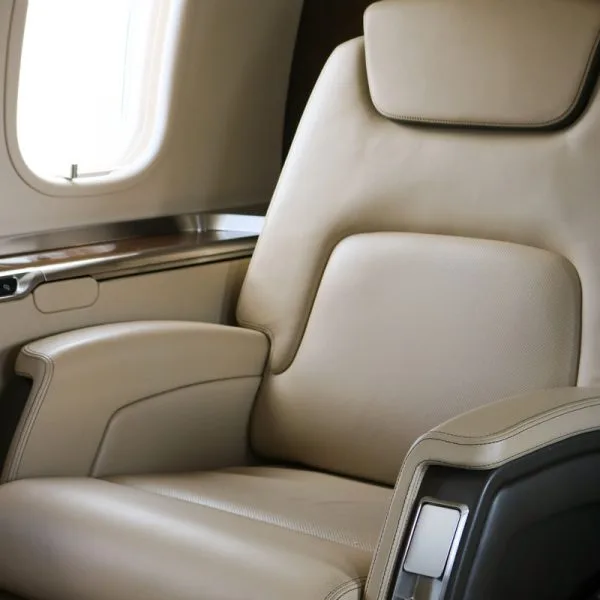 Close-up of a single beige leather aircraft seat next to a window.