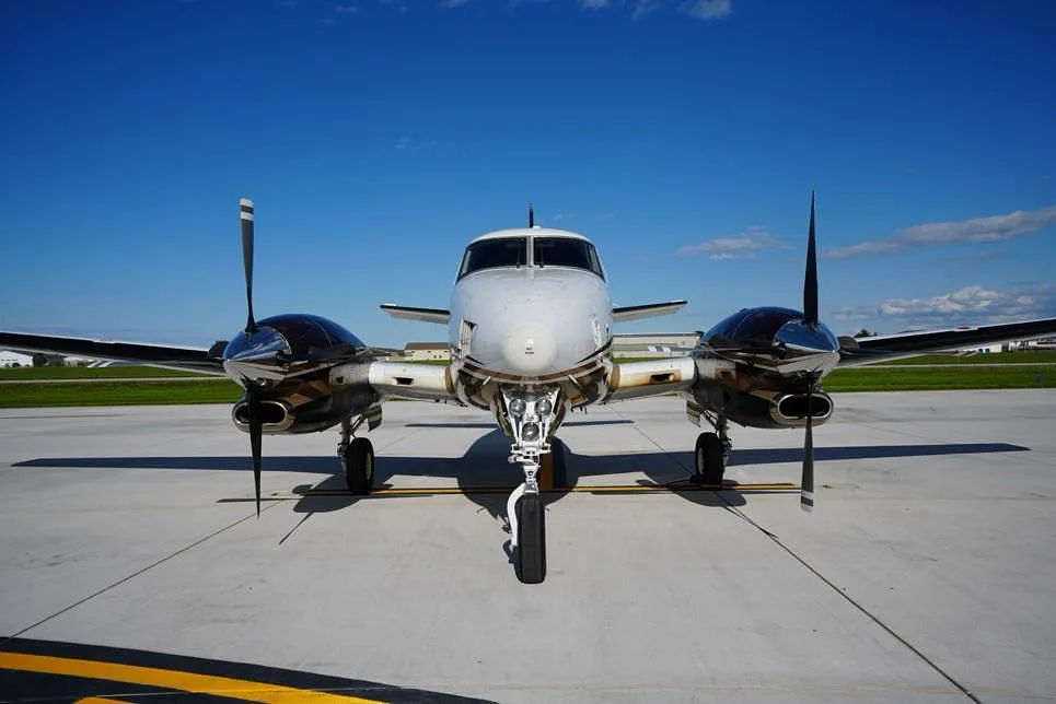 A head-on view of a white and brown Beechcraft King Air 200 parked on an airfield.