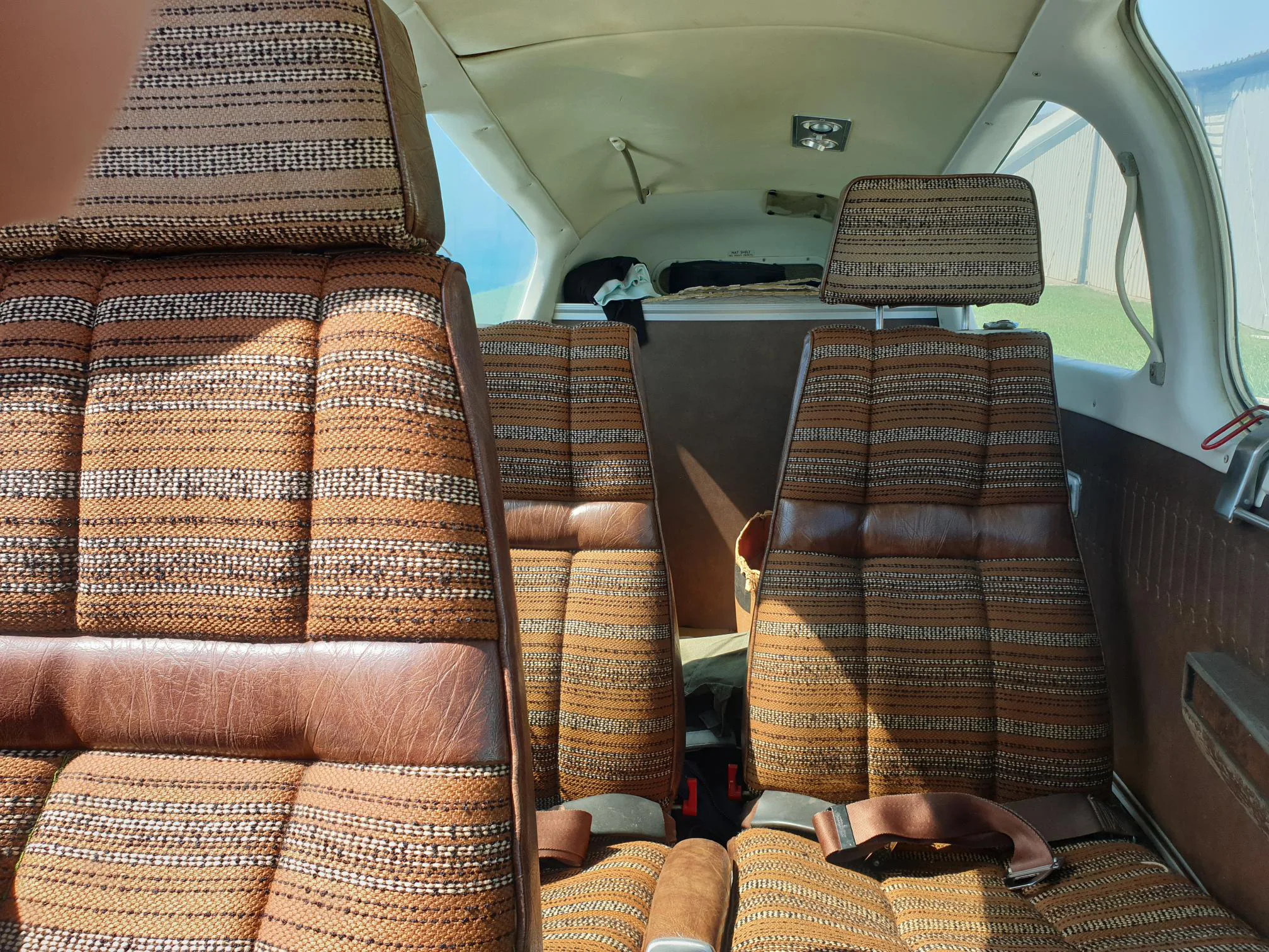 The interior cabin of a light aircraft, featuring brown and patterned fabric passenger seats.