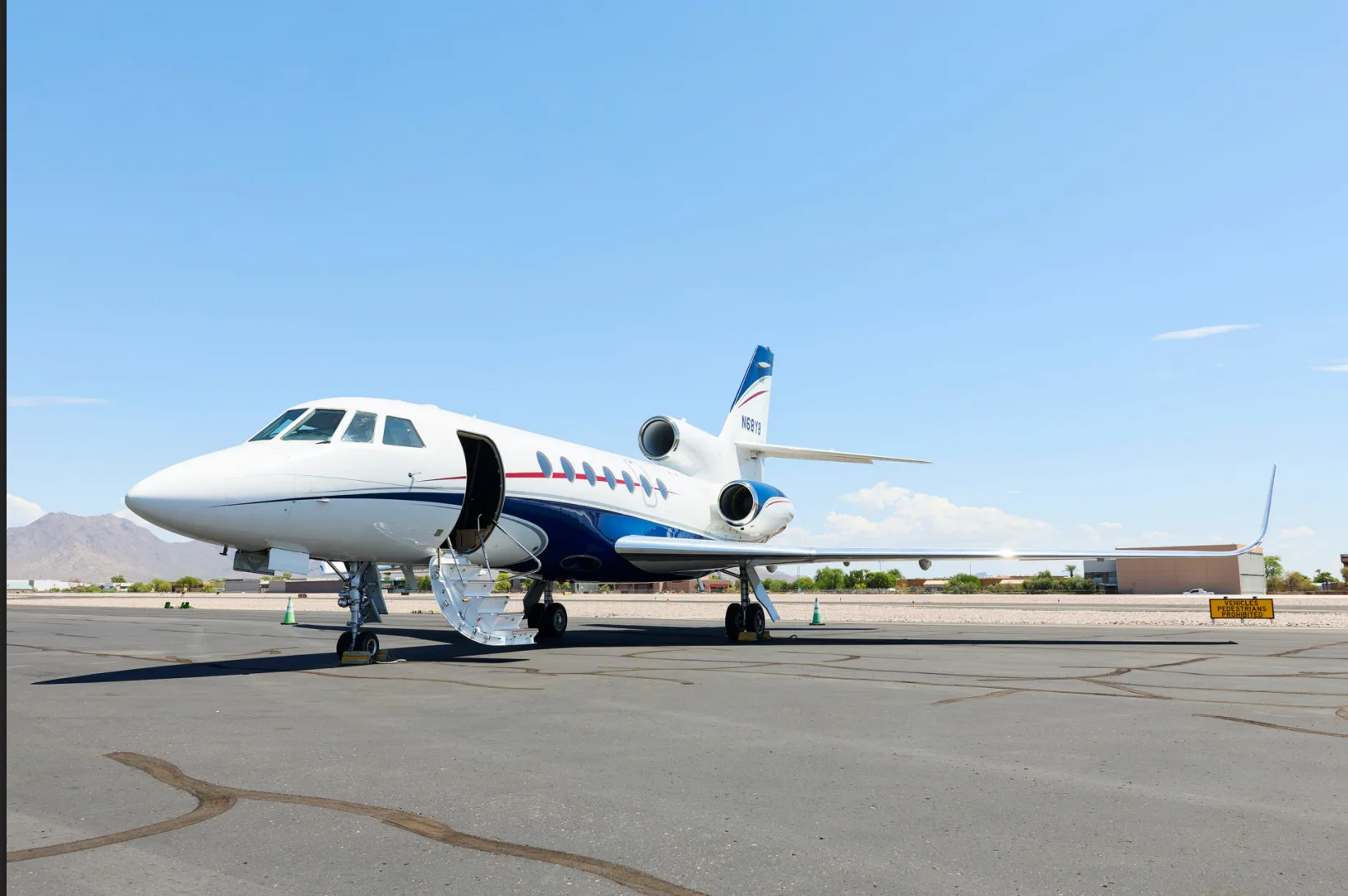 A white and blue business jet, N68YB, with its passenger door open and stairs deployed, is parked on an airport tarmac.