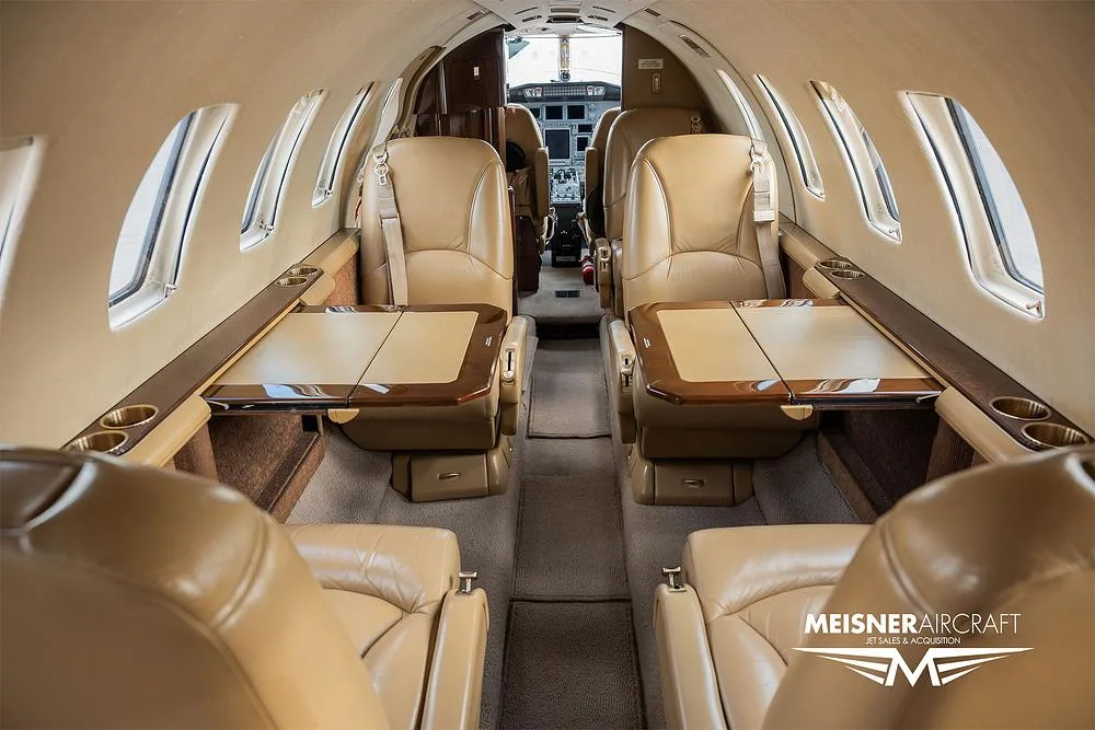 The interior cabin of a private jet with tan leather seats and fold-out tables deployed.