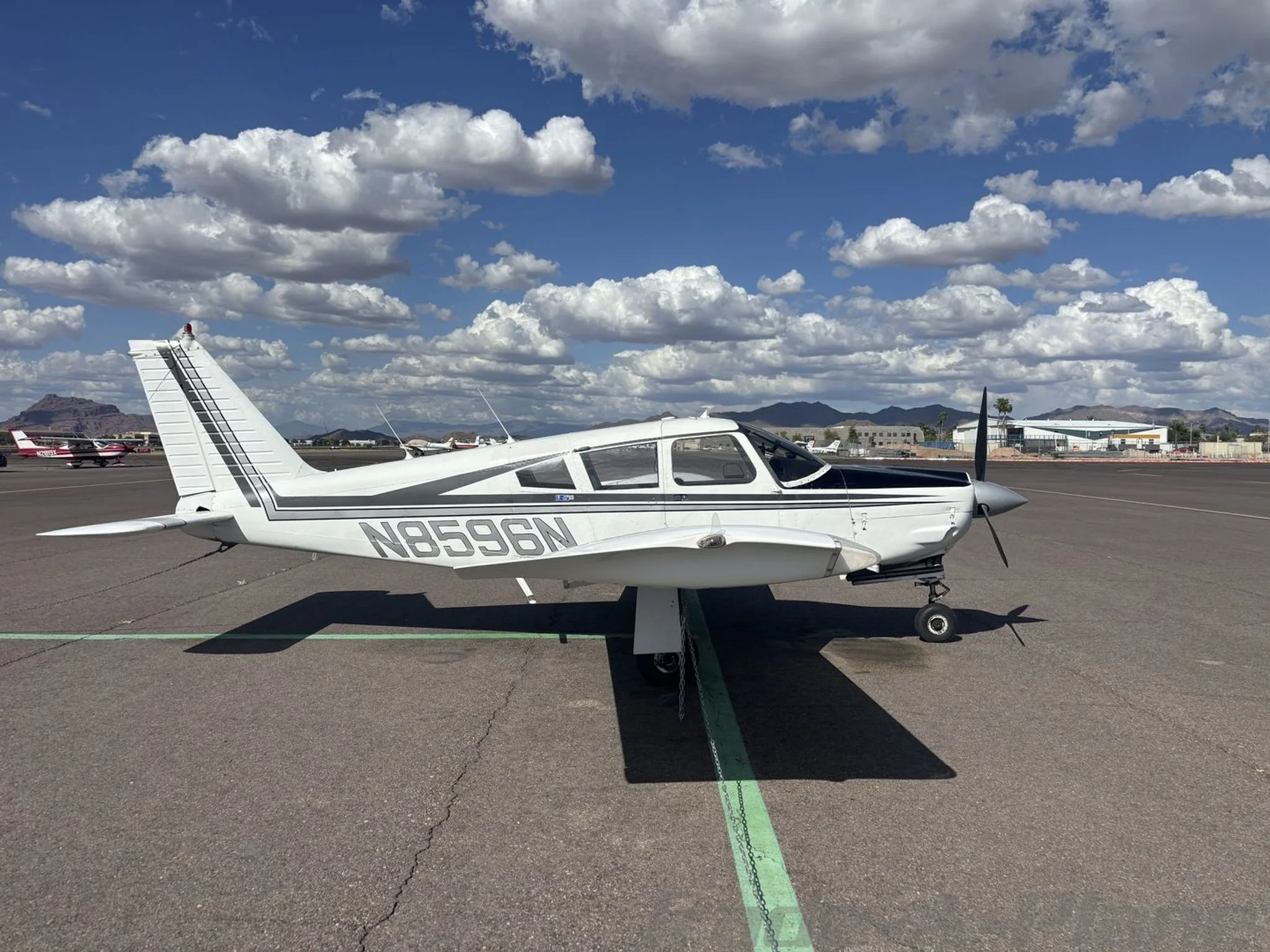 A white and black Piper Cherokee aircraft (N8596N) is parked on an airport tarmac with mountains in the background.