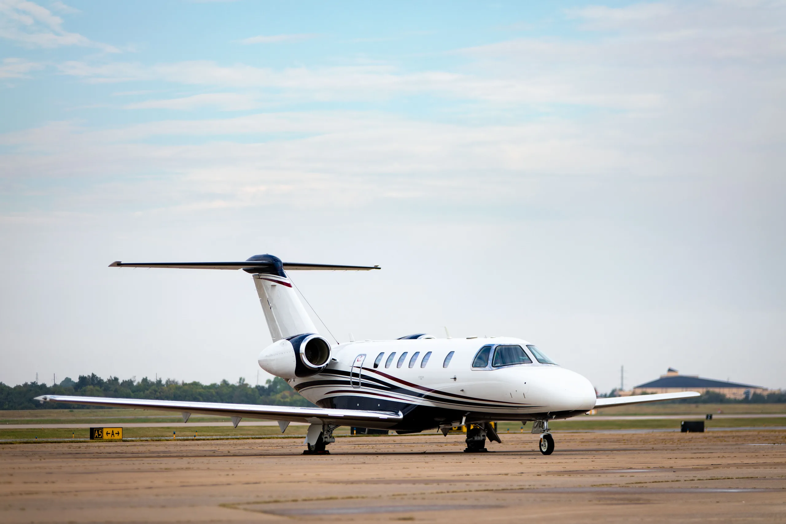 A white business jet with dark blue and gold stripes on the tarmac under a cloudy sky.