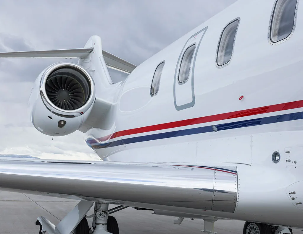 A close-up view of the engine, wing, and fuselage of a white business jet with red and blue stripes.