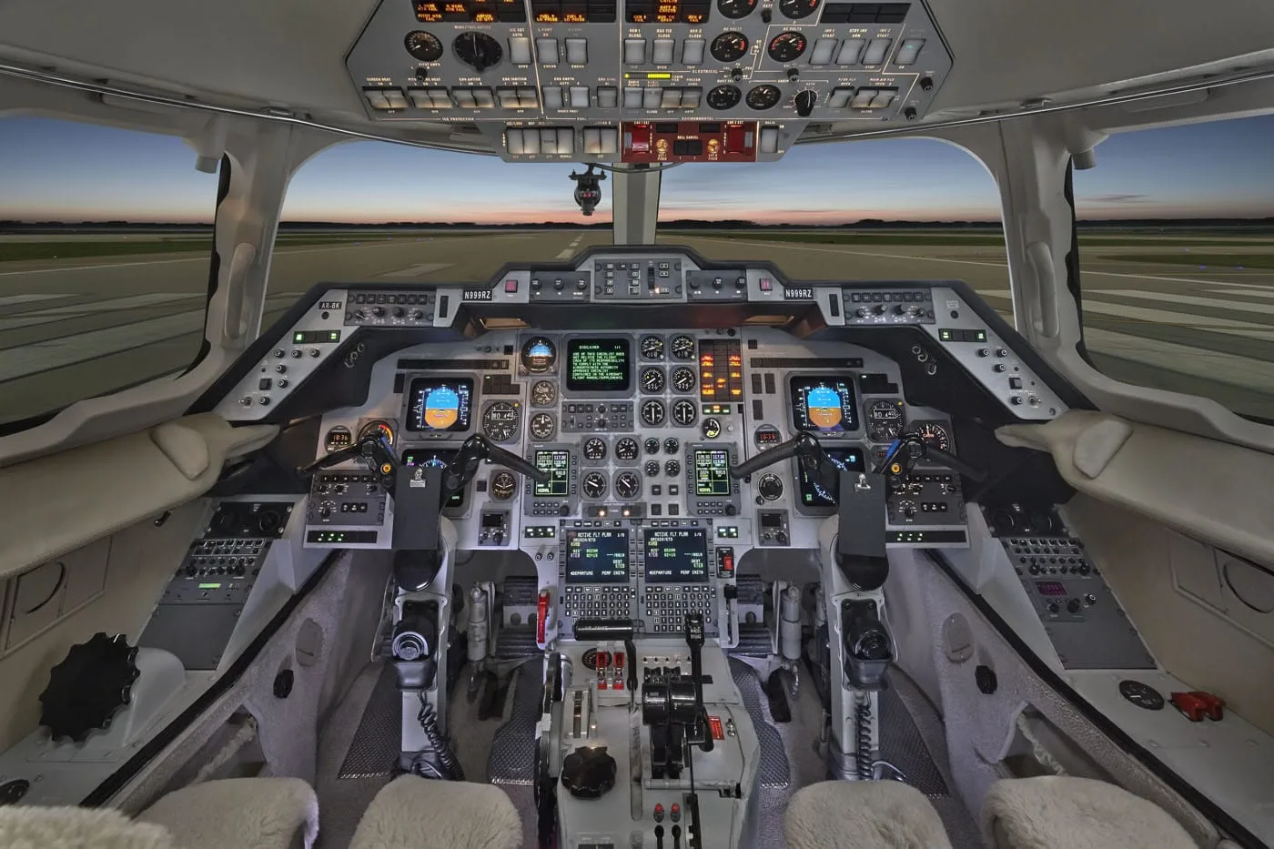 The cockpit of a business jet, featuring a complex instrument panel with multiple screens and controls, viewed from the pilot's seat.