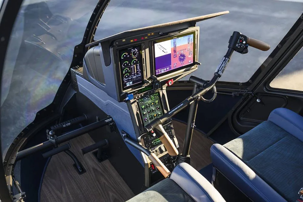 The modern cockpit of a helicopter featuring large digital displays, flight controls, and blue seats.