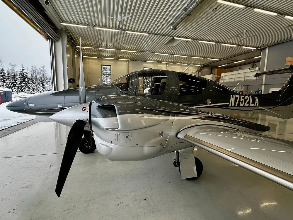 A side view of a gray and silver Diamond DA62 aircraft with registration N752LA, partially in a hangar with a snowy exterior visible.