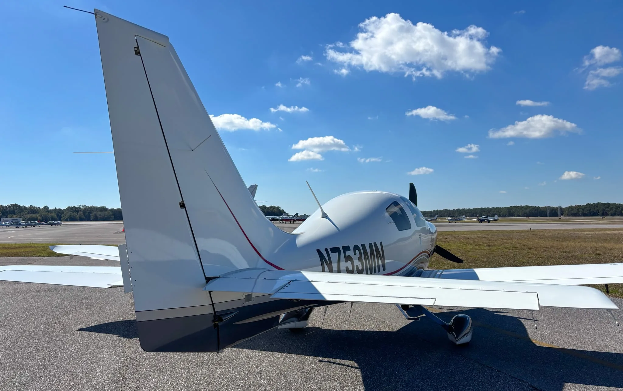 Rear view of the Lancair Columbia 400 N753MN with other aircraft visible in the distance on the runway.