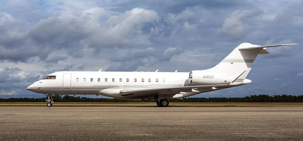 A white Bombardier Global Express business jet, registration N15GX, parked on a tarmac under a cloudy sky.