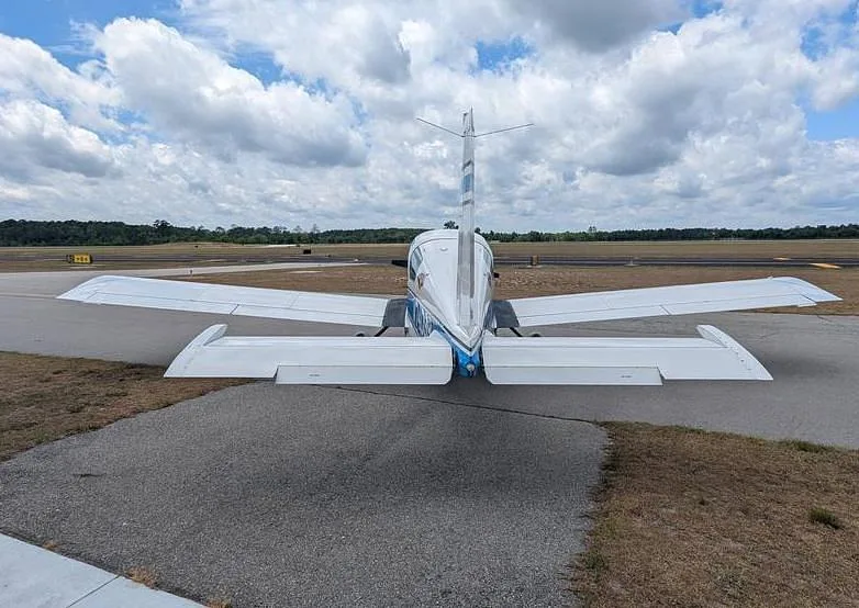 A rear view of the white and blue Grumman AA-5 Traveler N74099 showing its tail and wings on an airfield.