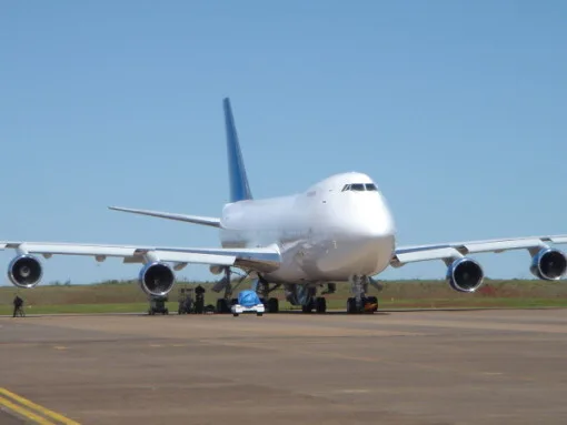 A front view of a large white Boeing 747 aircraft with blue tail accents parked on an airfield.