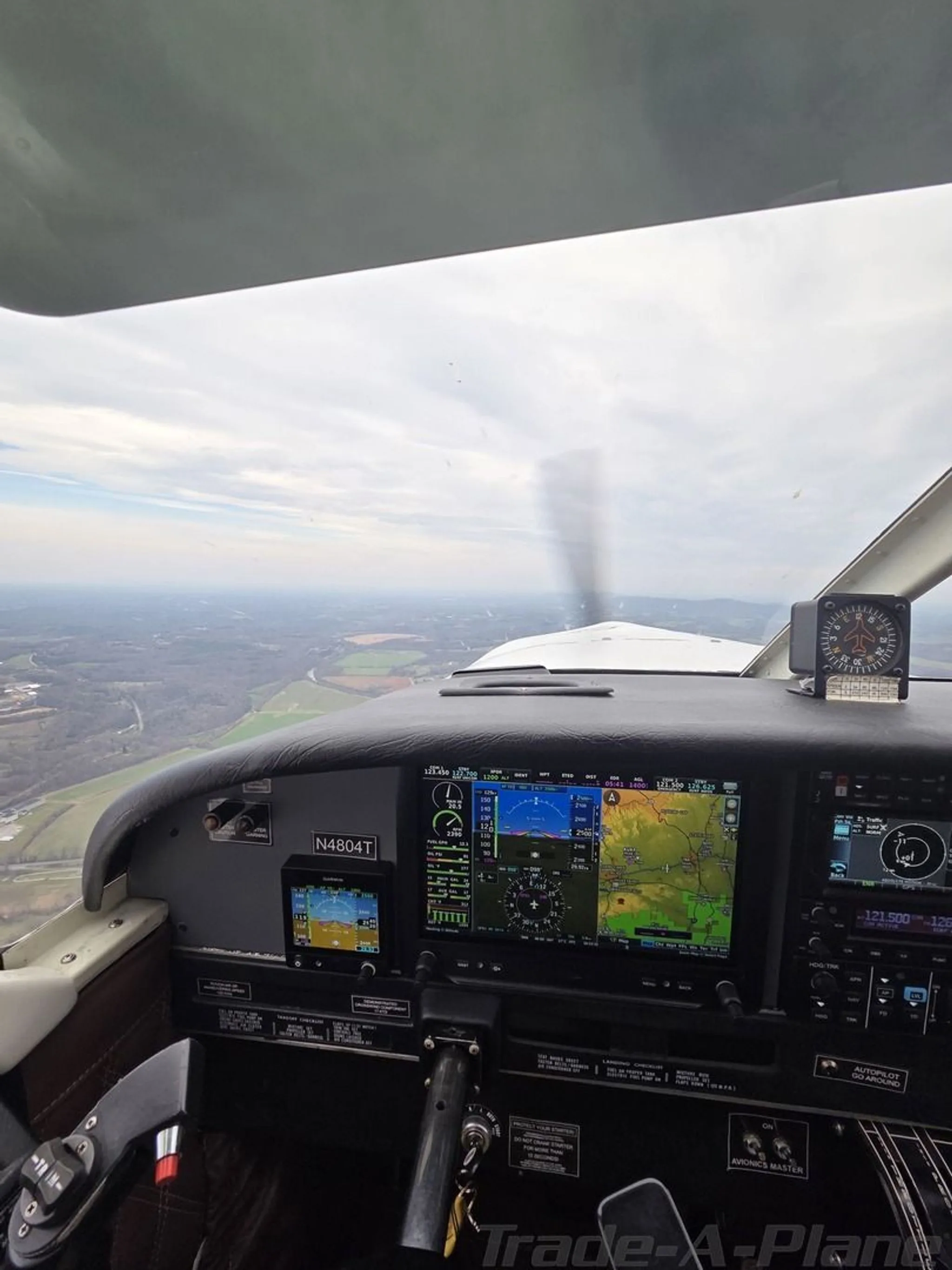 View from the cockpit of an aircraft in flight, showing the instrument panel and landscape below.