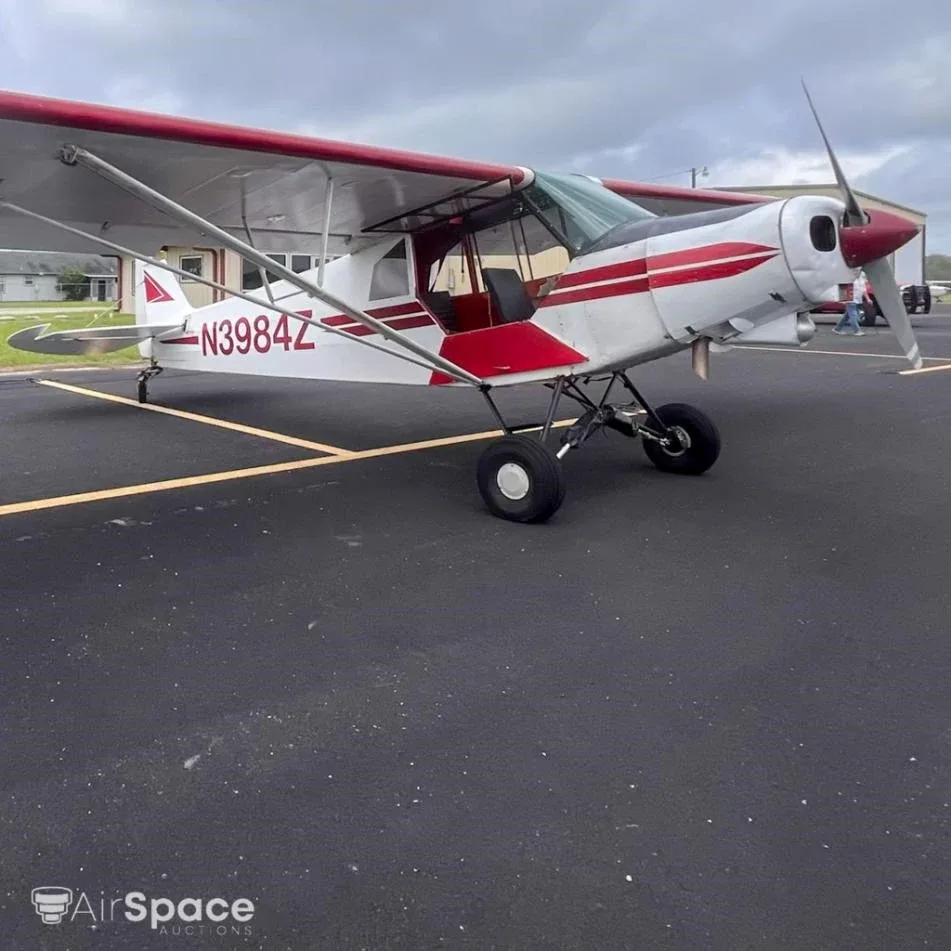A white high-wing aircraft with red stripes, registration N3984Z, parked on an asphalt apron with its door open.