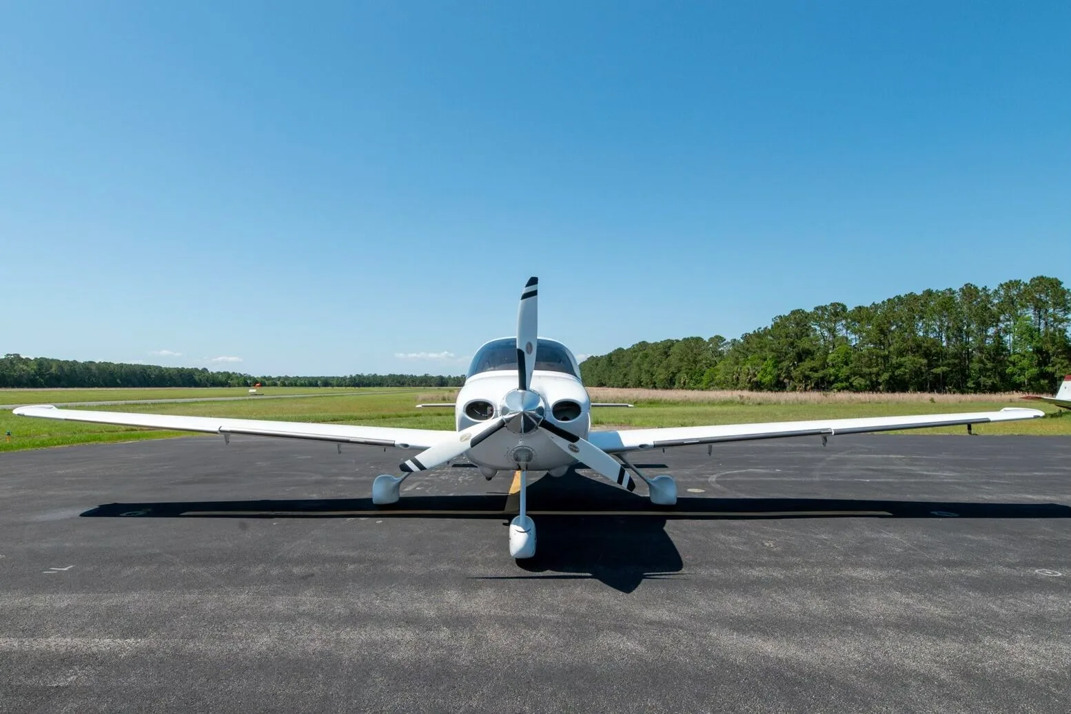 Front view of a white Cirrus SR22T aircraft N717PG with a three-bladed propeller on an airfield.