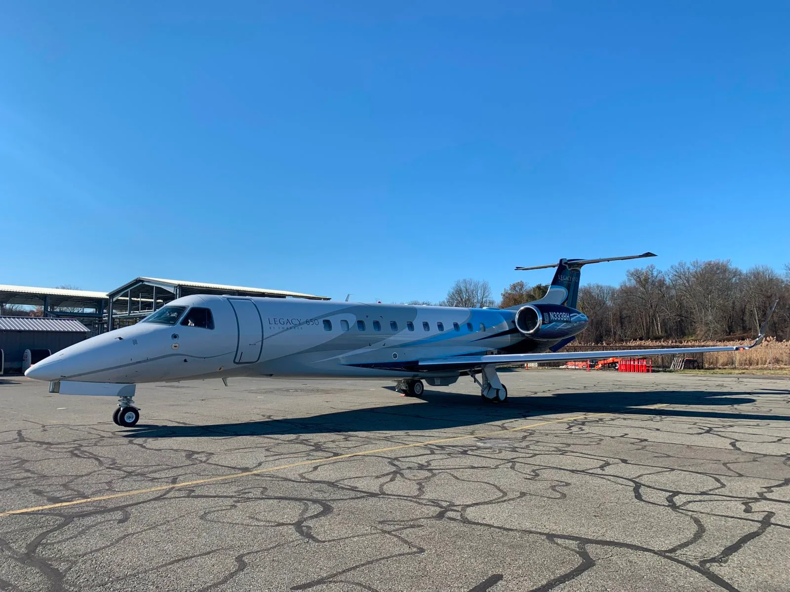 A grey and blue Embraer Legacy 650 business jet with registration N339BH is parked on an asphalt tarmac under a clear blue sky.